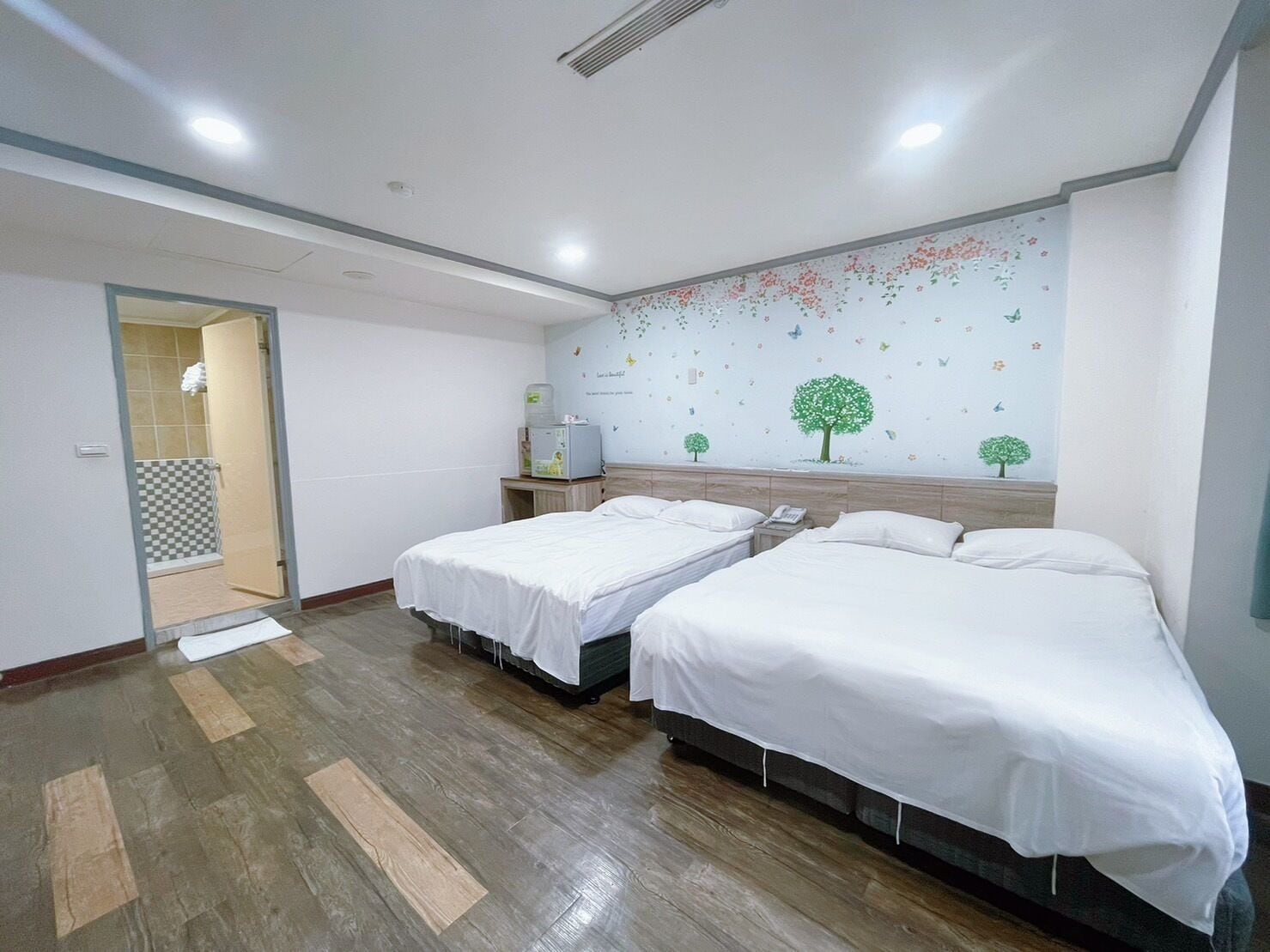 A hotel room with two beds, a shower area, and a wall decorated with nature-themed stickers.