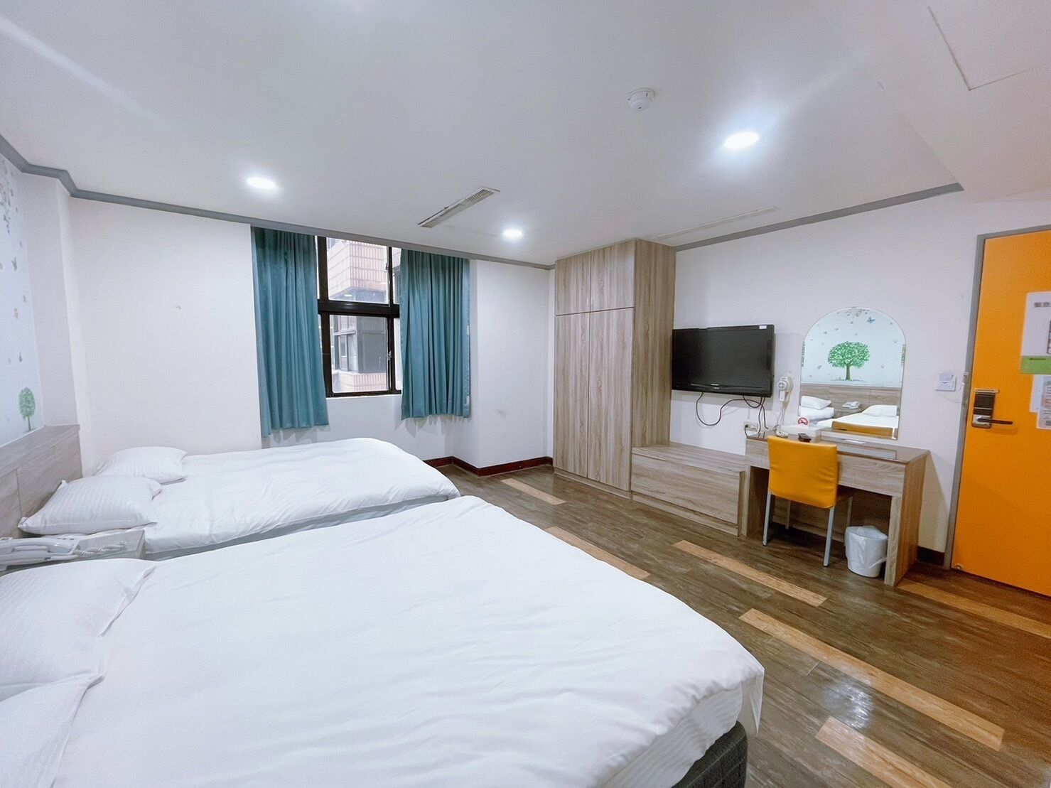 A hotel room with two beds, a desk, a TV, and a bathroom.