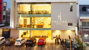 Ett modernt hotell med en tydlig skylt som visar namnet ”The One Hotel”, flera våningar och en parkeringsplats med olika typer av fordon.