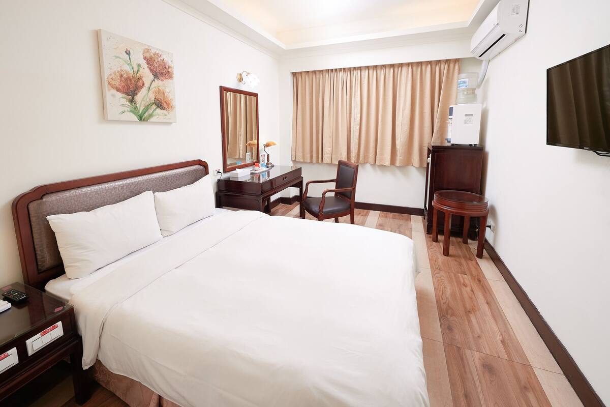 A hotel room with a large bed, a desk with a chair, a television, and a painting on the wall.
