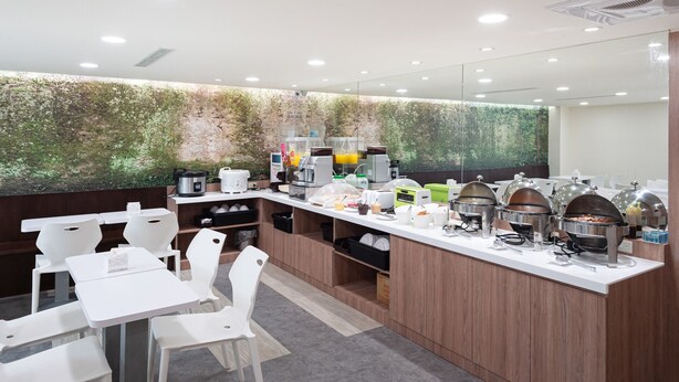 A modern breakfast bar with white chairs, a coffee station, and a green wall with a nature mural. - Peach Hotel (Hsinchu)