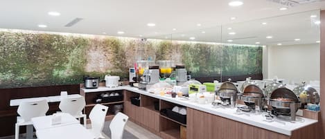 Um balcão de café da manhã moderno com cadeiras brancas, uma estação de café e uma parede verde com um mural da natureza.