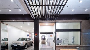 A hotel entrance with a parked car, a bench, and a sign for the Peach Hotel. - Peach Hotel (Hsinchu)