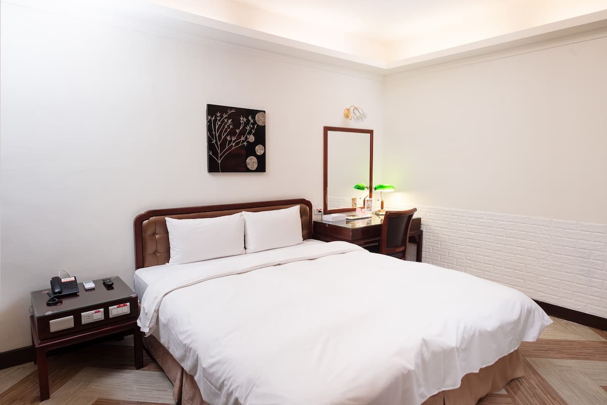 A neatly arranged hotel room with a bed, bedside table, lamp, and a wall-mounted artwork.