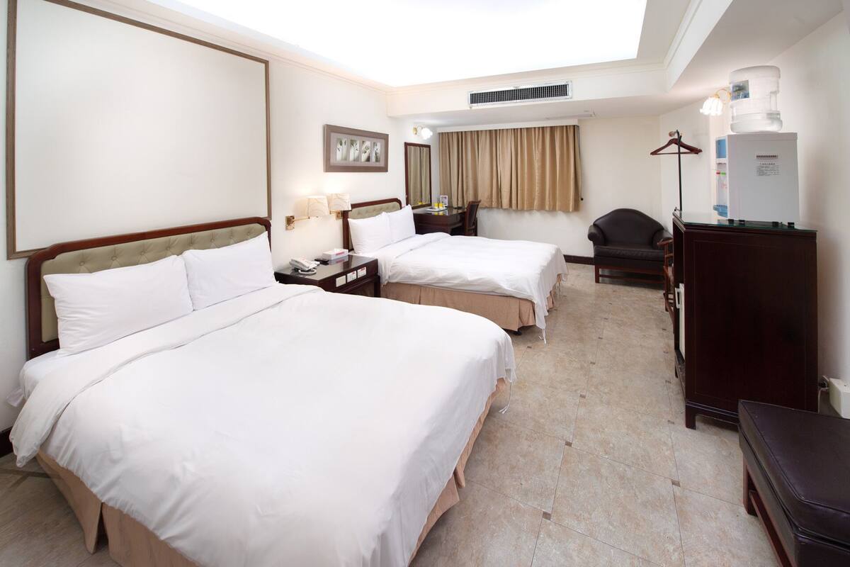 A hotel room with two beds, a desk, a chair, a wardrobe, and a water dispenser.