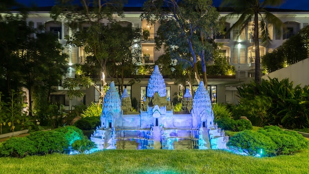 A nighttime view of a well-lit temple-like structure surrounded by lush greenery and a modern building in the background. - Damrei Angkor Hotel (Siem Reap)