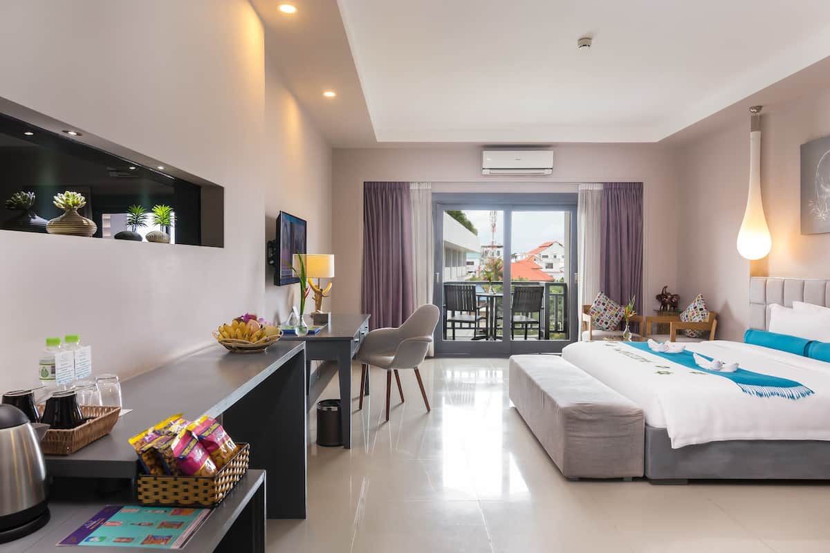 A modern hotel room with a bed, a desk with breakfast items, a balcony with a view, and a TV on the wall.