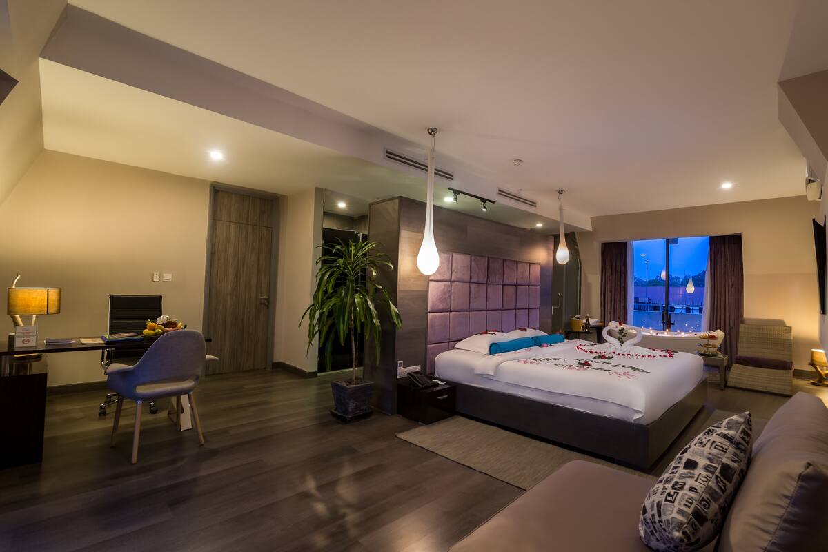 A modern hotel room with a large bed, a desk, a chair, and a potted plant.