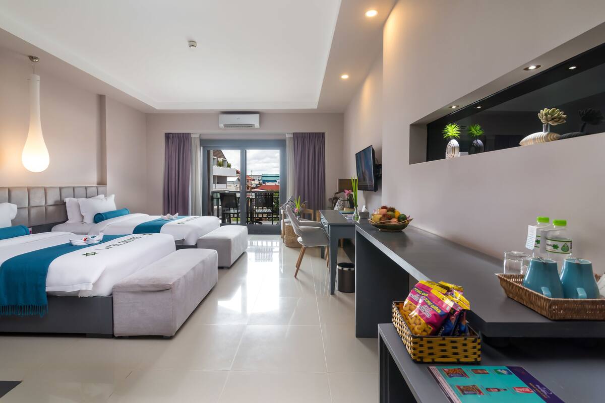 A modern hotel room with two beds, a dining area, and a balcony with a view.
