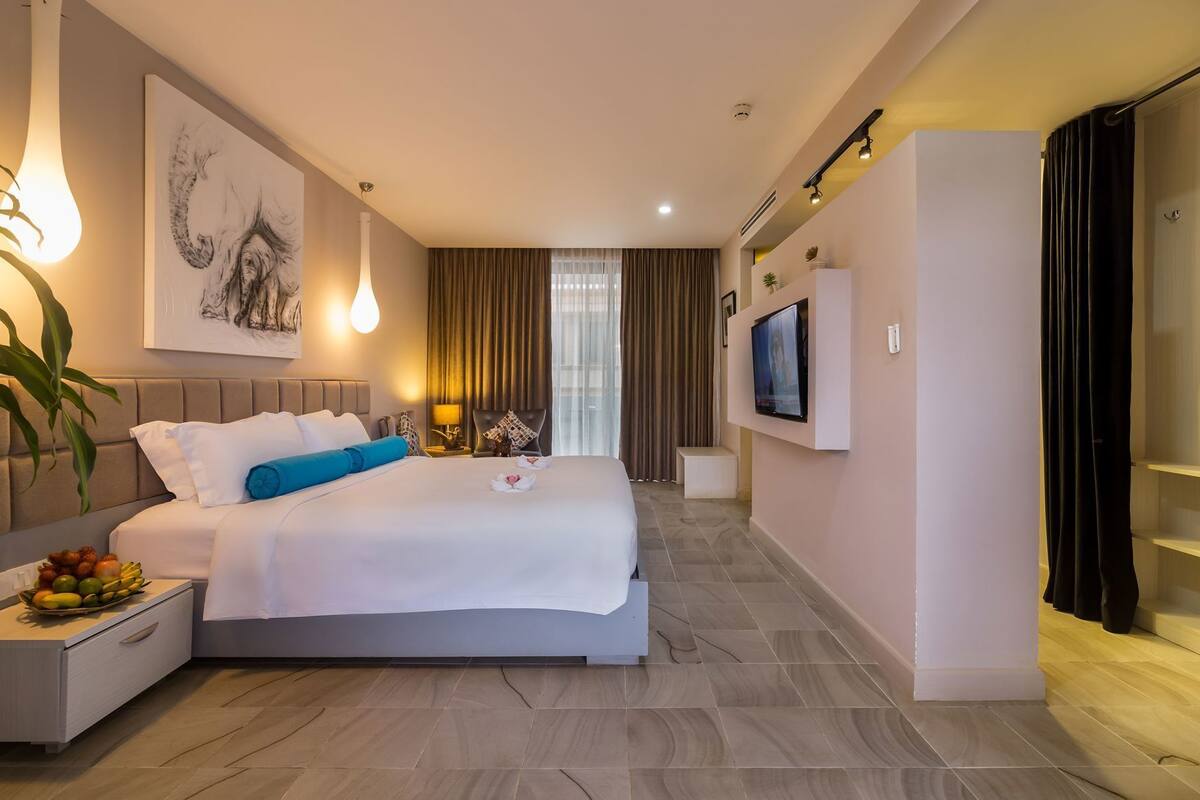 A hotel room with a bed, bedside table, TV, and a large window with curtains.
