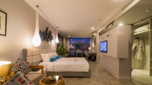 A modern hotel room with a large bed, bedside table, lamp, and a TV. There is a seating area with a table and chairs, and a robe hanging on the wall. - Damrei Angkor Hotel (Siem Reap)