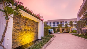 A paved walkway leading to a building with a stone wall and a row of parked cars. - Damrei Angkor Hotel (Siem Reap)