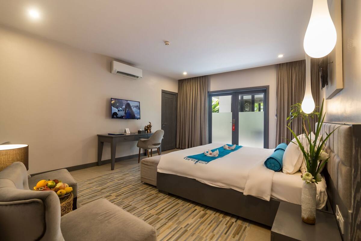 A hotel room with a bed, desk, TV, and a view through a door.