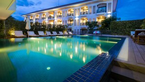 A swimming pool with lounge chairs, a building with multiple balconies, and a well-lit facade. - Damrei Angkor Hotel (Siem Reap)