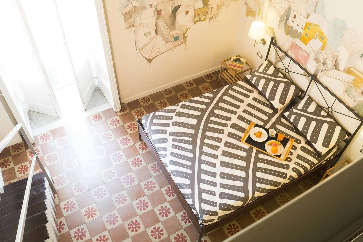 A bedroom with a bed, a nightstand, a lamp, and a wall mural.