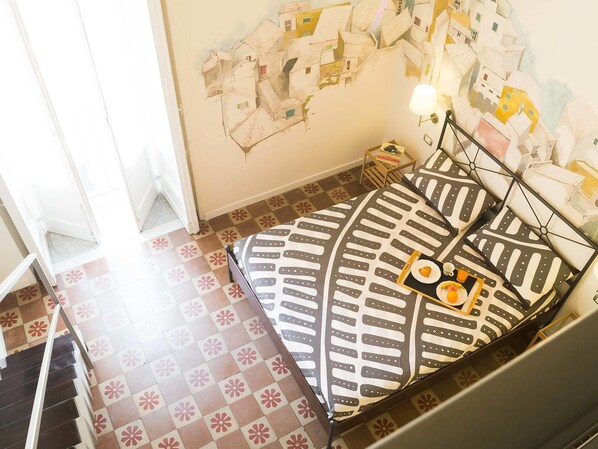 Un dormitorio con cama, mesita de noche, lámpara y un mural en la pared.