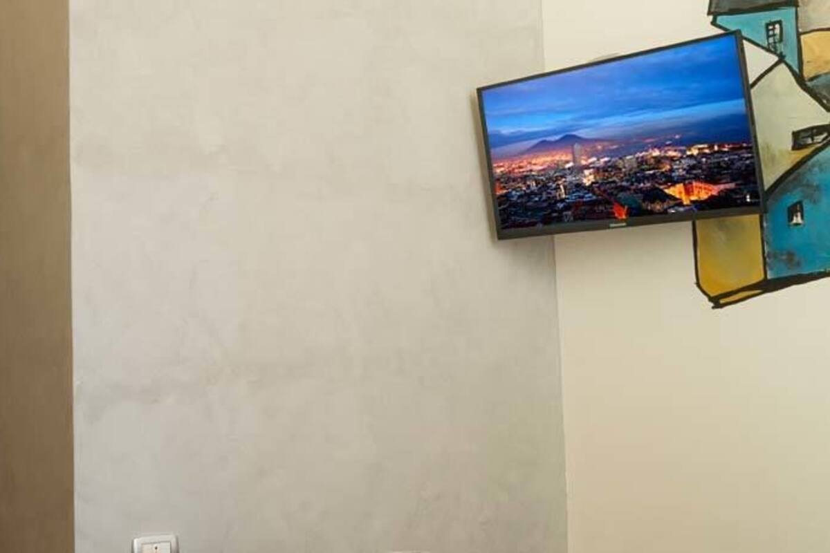 A hotel room with a large flat-screen TV mounted on the wall, a decorative panel with intricate patterns, and a view of a cityscape at dusk.