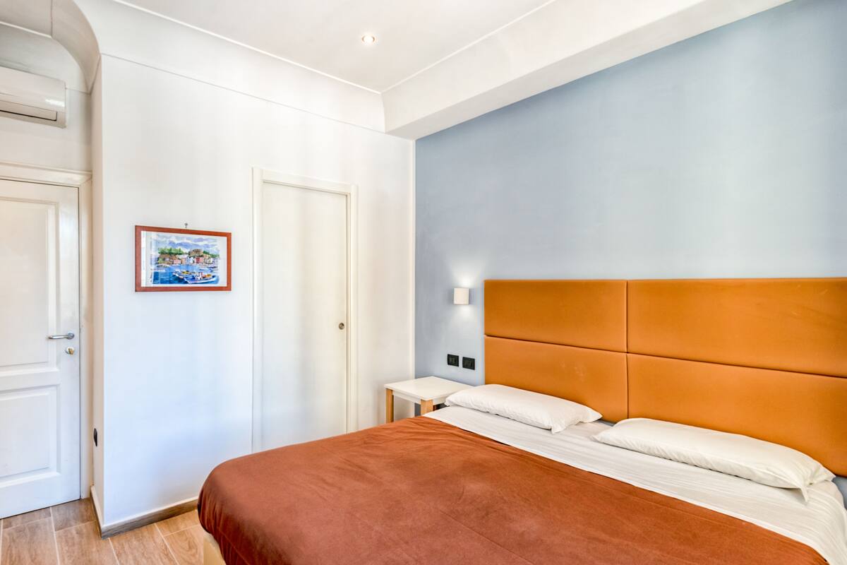 Een slaapkamer met een bed, een nachtkastje, een ingelijste foto aan de muur en een deur.