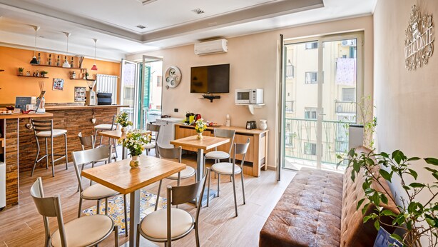 Een moderne woonkamer met een bank, eettafel en stoelen. Er is een keuken met een aanrecht en apparatuur. Een televisie is aan de muur bevestigd en er is een balkon met uitzicht op de stad.