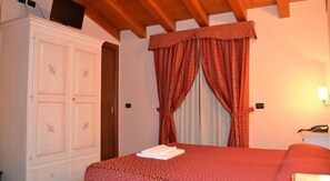 A bedroom with a large wardrobe, a bed with a red bedspread, and a window with red curtains.