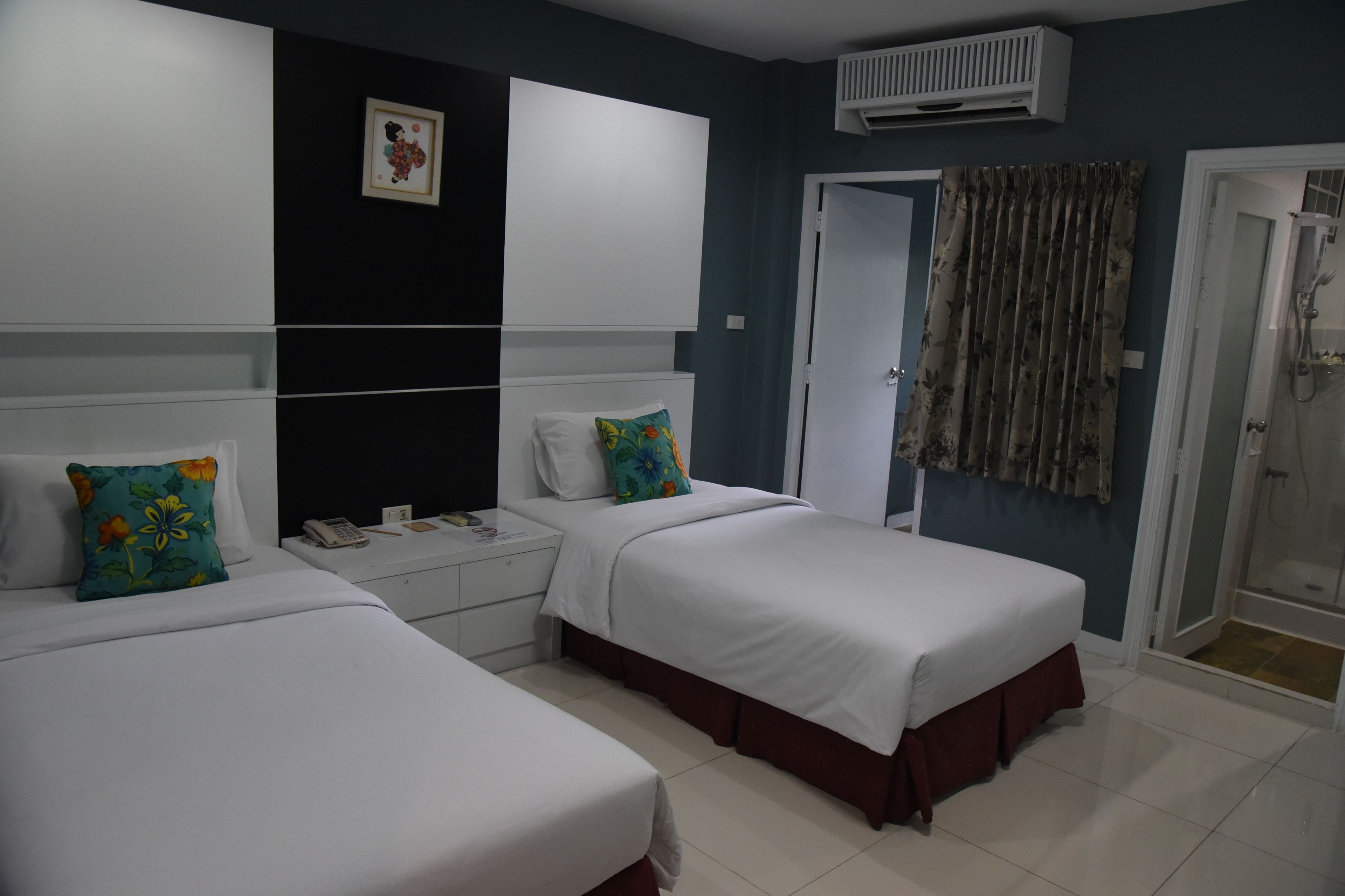 A hotel room with two beds, a white wardrobe, a bedside table with a phone, and a shower area.