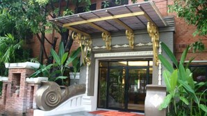 A building entrance with a covered porch, a large decorative sculpture, and lush greenery.