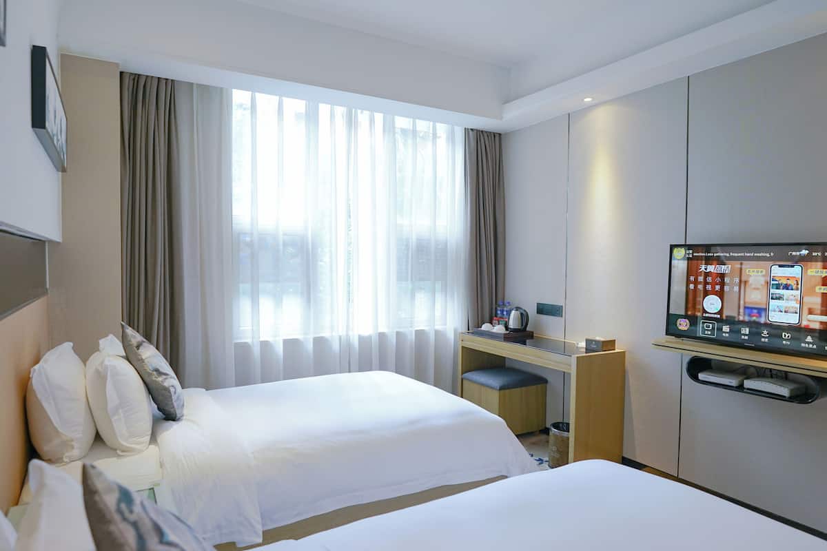 A hotel room with two beds, a desk with a computer, a TV, and a window with curtains.
