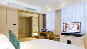 A hotel room with a large bed, a desk with a flat-screen TV, a mirror, and a door leading to a bathroom. - Paco Hotel Tiyuxilu Metro Guangzhou (Guangzhou)
