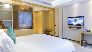 Habitación de hotel con una cama grande, televisor montado en la pared, una mesita y una ventana con cortinas.