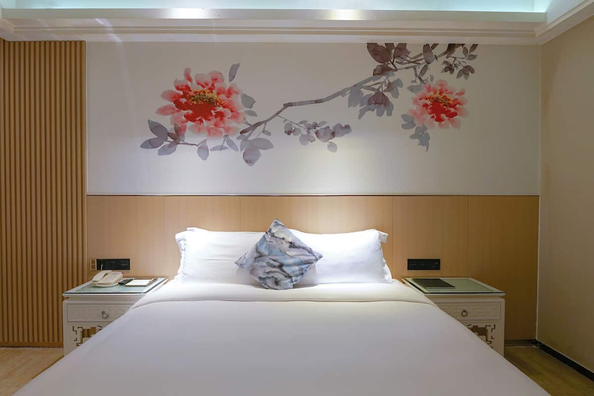 A hotel room with a large bed, two bedside tables, a wall-mounted phone, and a decorative floral painting.