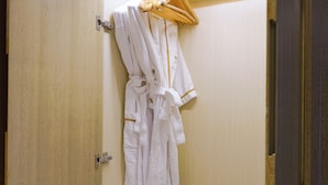Un baño de hotel con una bata colgada en un perchero, pantuflas en el suelo y una mesita con artículos de aseo.