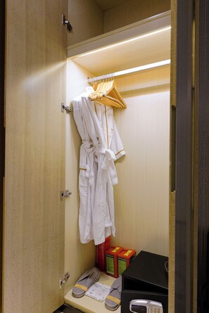 A hotel bathroom with a robe hanging on a rack, slippers on the floor, and a small table with toiletries. - Paco Hotel Tiyuxilu Metro Guangzhou (Guangzhou)