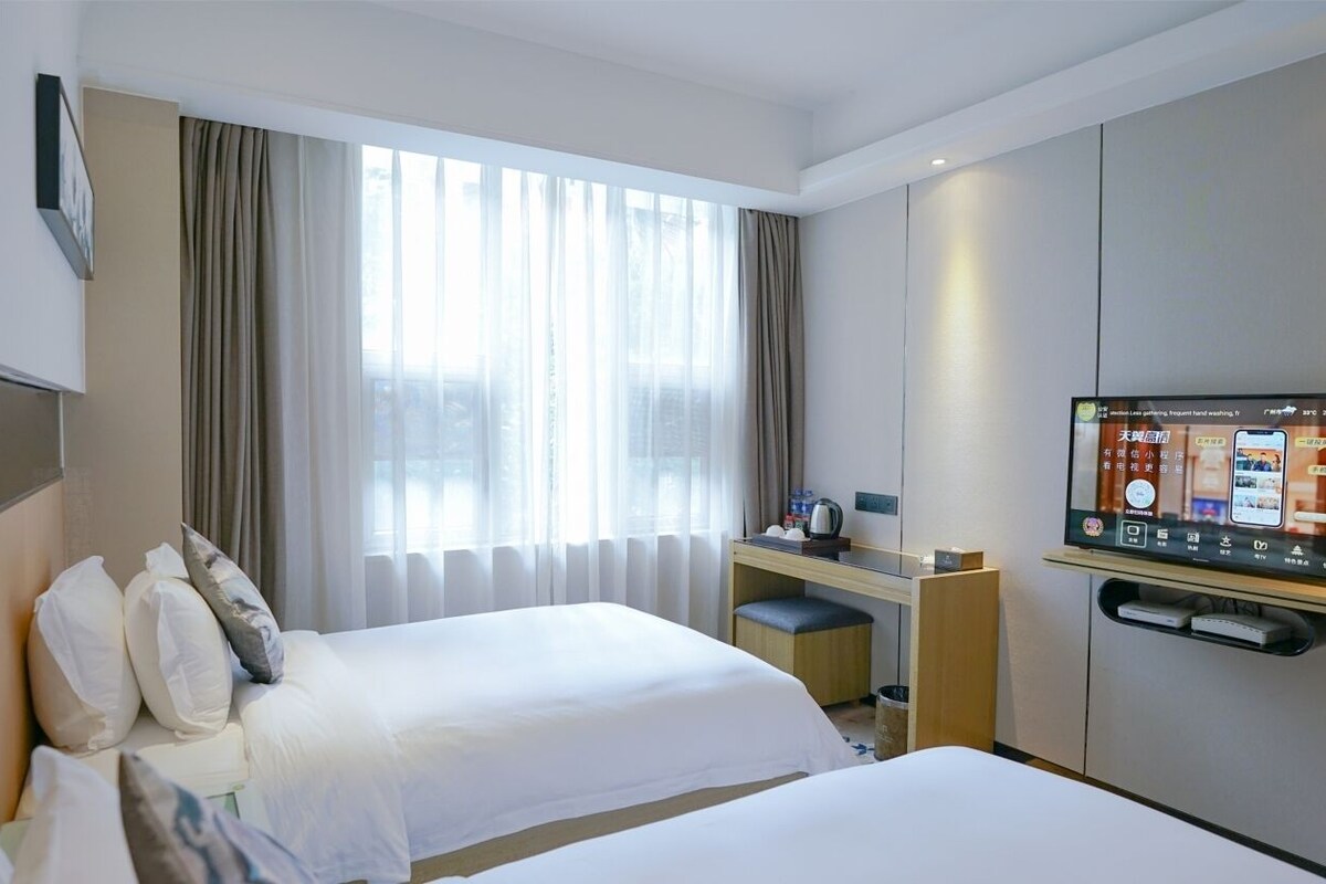 Een hotelkamer met twee bedden, een bureau, een televisie en een raam met gordijnen.
