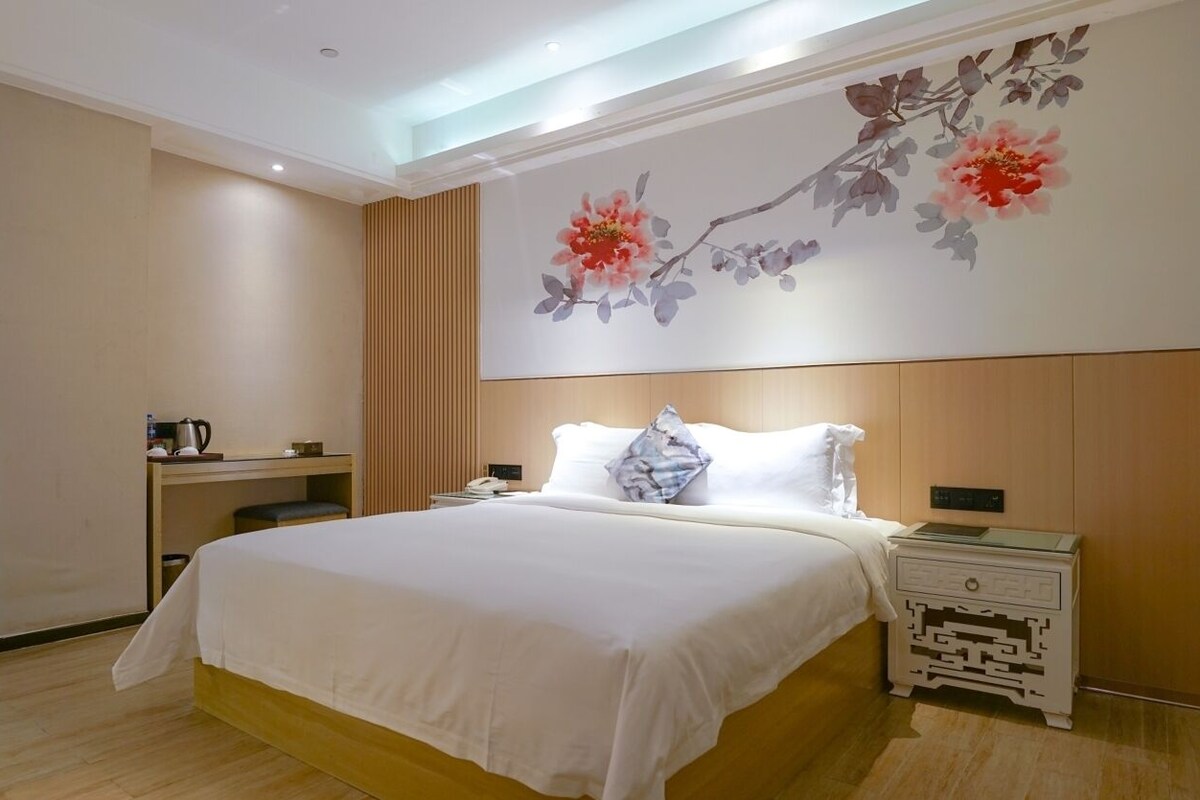 Een hotelkamer met een groot bed, nachtkastjes, een wandlamp en een bloemenmural.