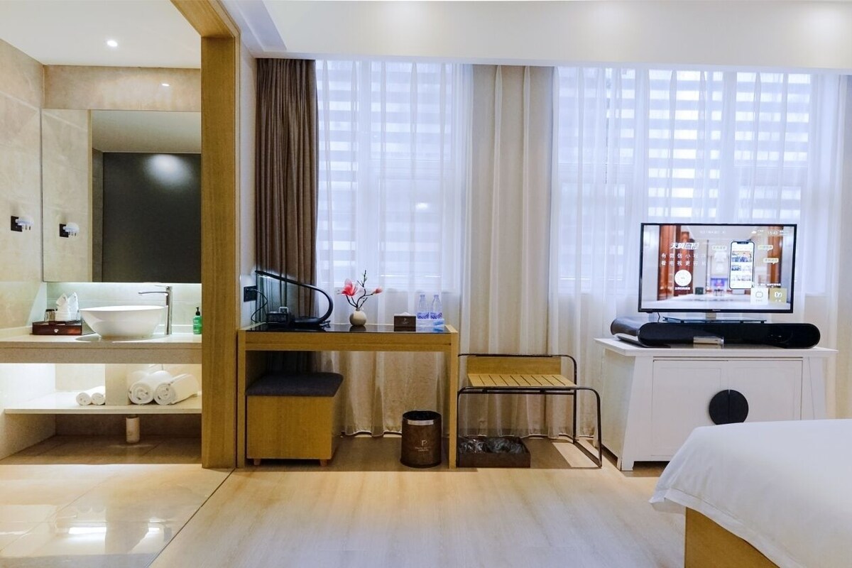 Hotelkamer met een bed, bureau met stoel, televisie, raam met gordijnen en een badkamerruimte.