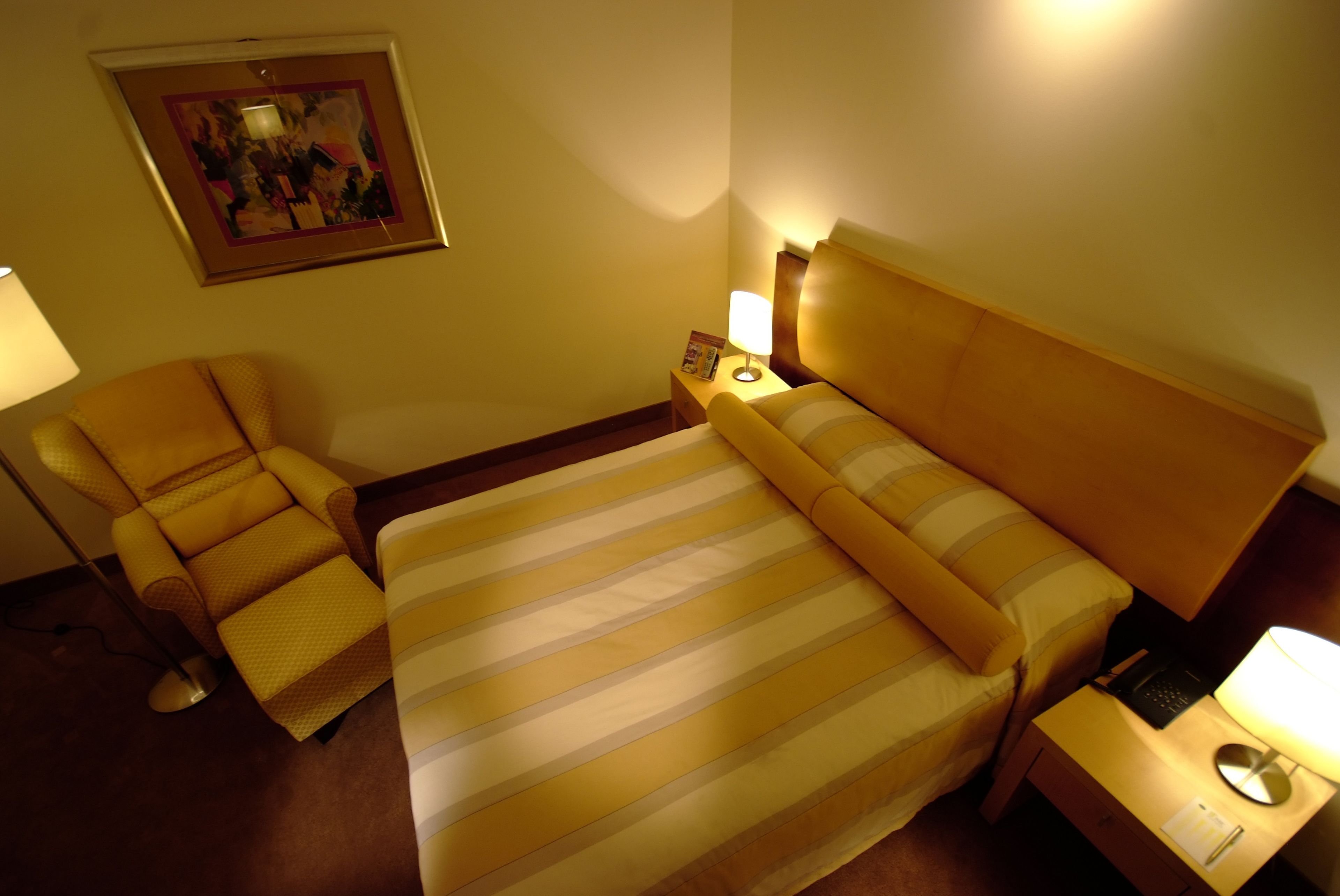 A hotel room with a bed, a chair, a nightstand, and a lamp.