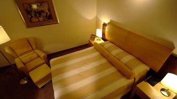 A hotel room with a bed, a chair, a nightstand, and a lamp.