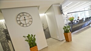 A reception area with a wall-mounted clock, two potted plants, and a reception desk. - Hotel Hp Park (Poznan)