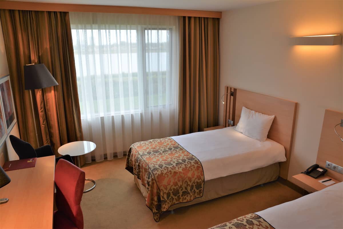 A hotel room with a bed, a desk, a chair, a small table, and a window with curtains.