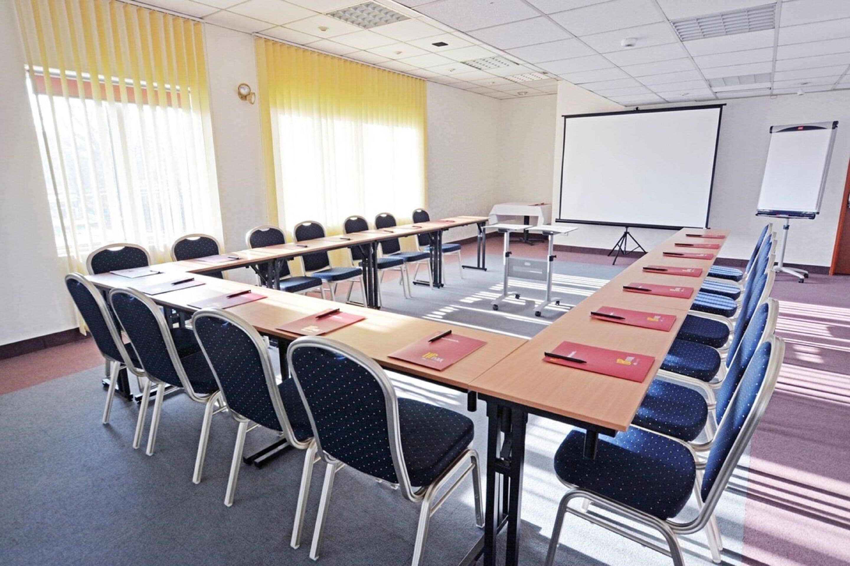 A conference room with a long table, chairs, a projector screen, and a whiteboard.