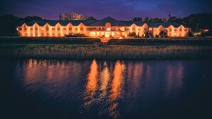 A large, illuminated hotel with a symmetrical facade and a reflection in the water in front. - Hotel Hp Park (Poznan)