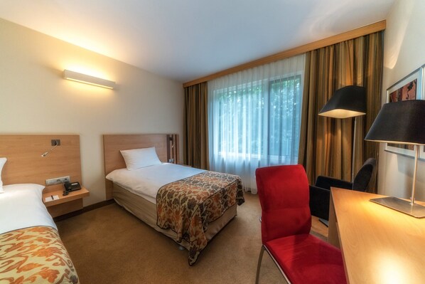 A hotel room with a bed, a desk, a chair, a nightstand, and a lamp.