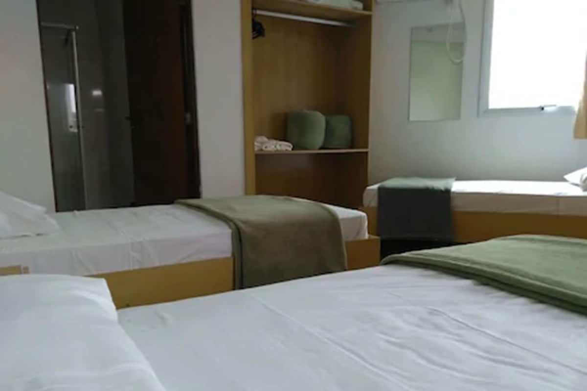 A dormitory room with two single beds, a wardrobe, a mirror, and a window.