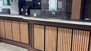 A reception desk with a wooden panel design, a digital screen, and a sign with a warning symbol. - Hotel Family (São Paulo)