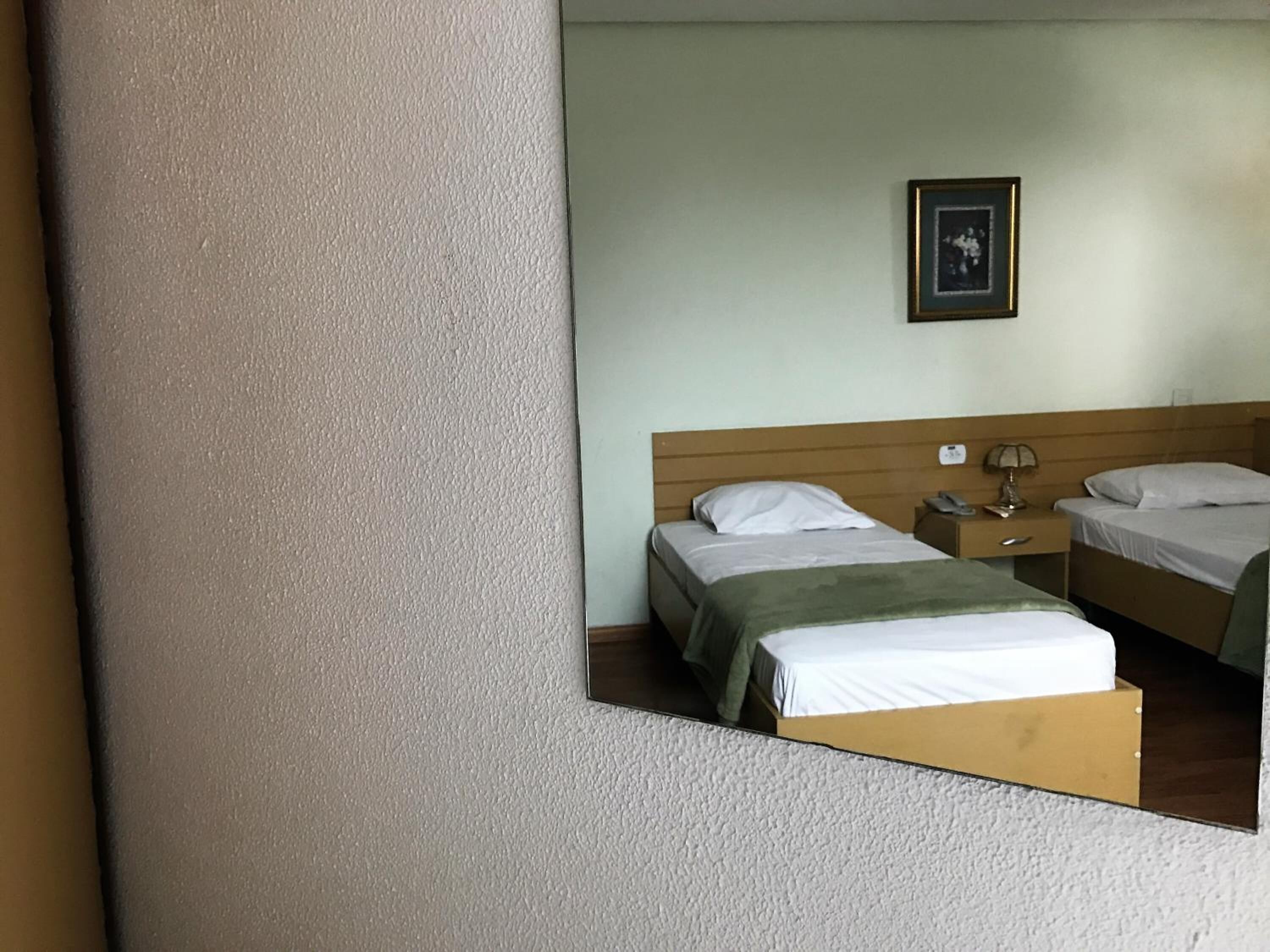 Habitación de hotel con dos camas, una mesita de noche con lámpara, un cuadro enmarcado en la pared y un cabecero de madera.