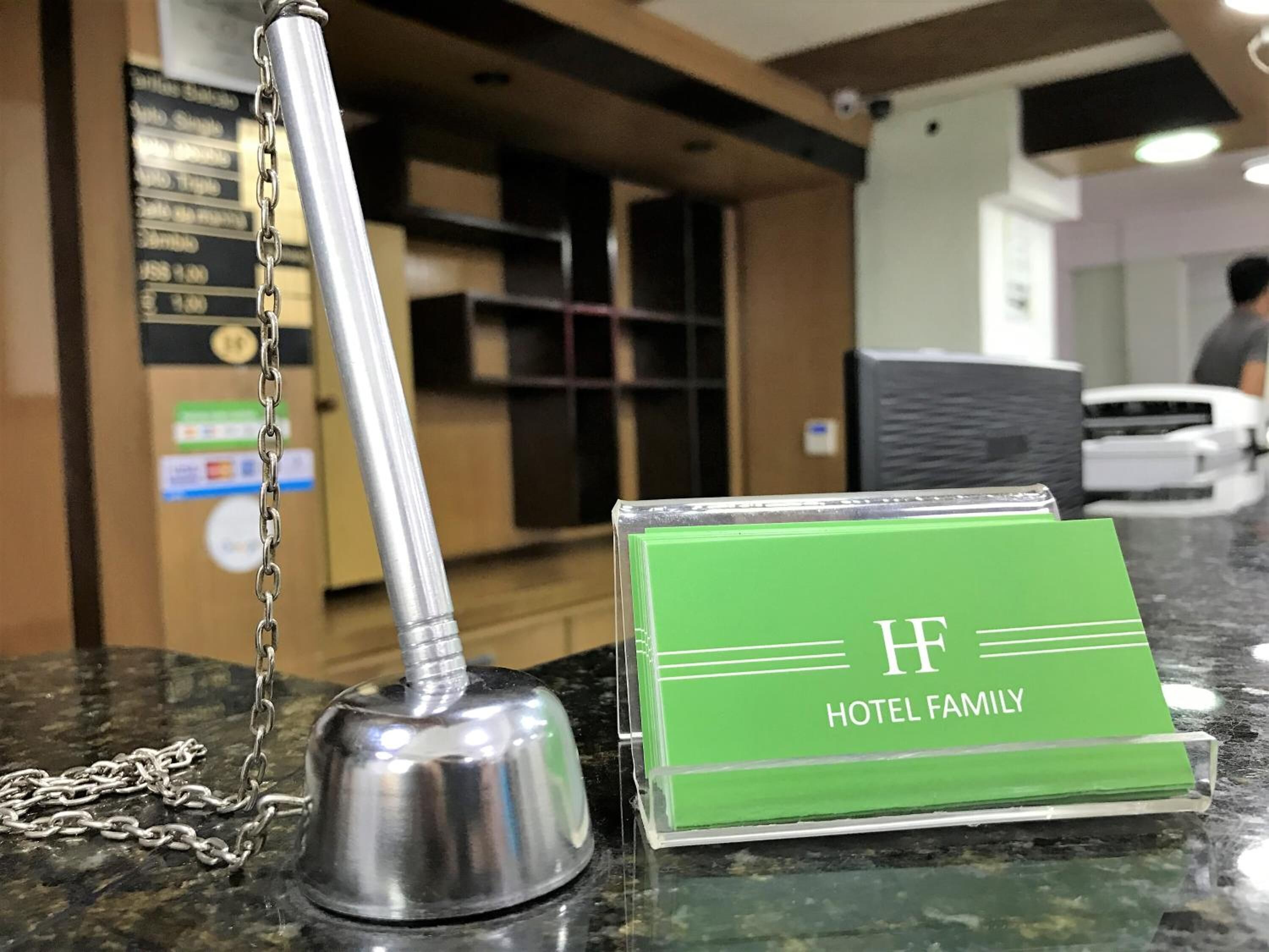 Un espace d’accueil d’hôtel avec une enseigne verte indiquant « HÔTEL POUR FAMILLES », une cloche argentée et une chaîne.