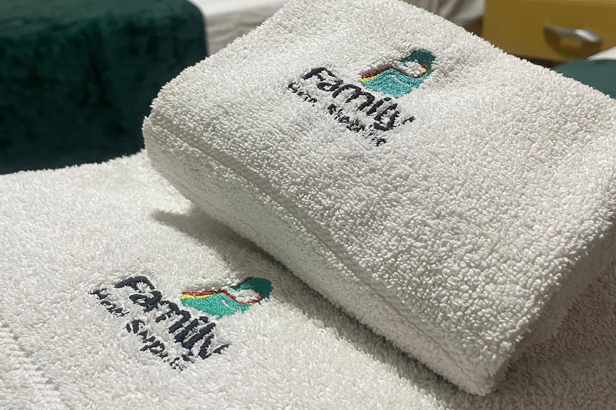 A neatly folded white towel with embroidered text and a logo, placed on a bed in a hotel room.