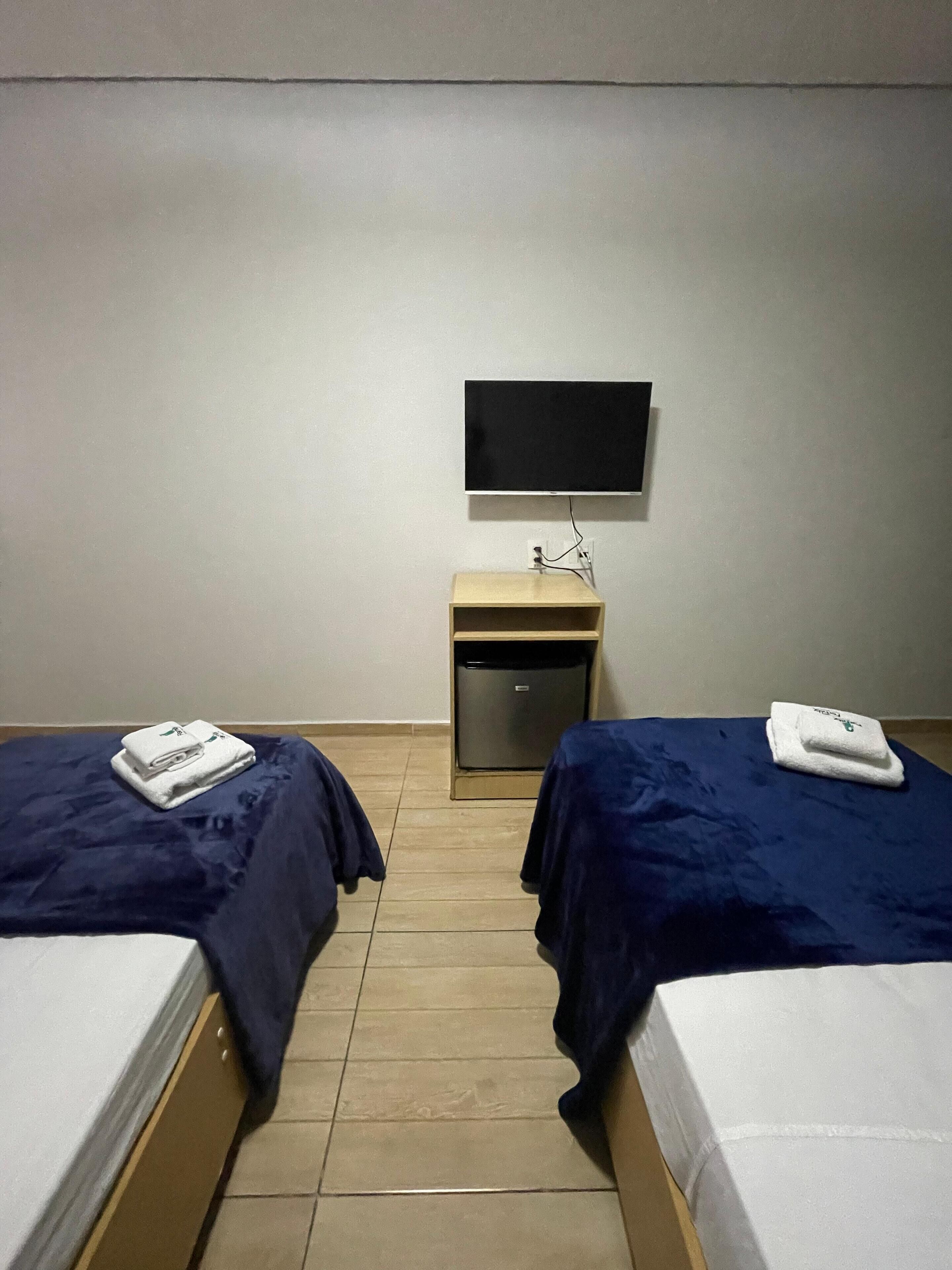A hotel room with two beds, a small desk, a television, and a compact refrigerator.