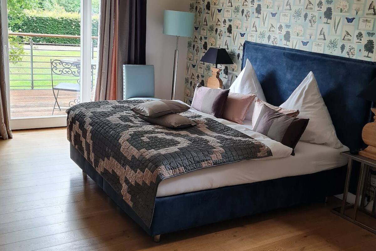 A bedroom with a large bed, a view to the outside, and a patterned wallpaper.
