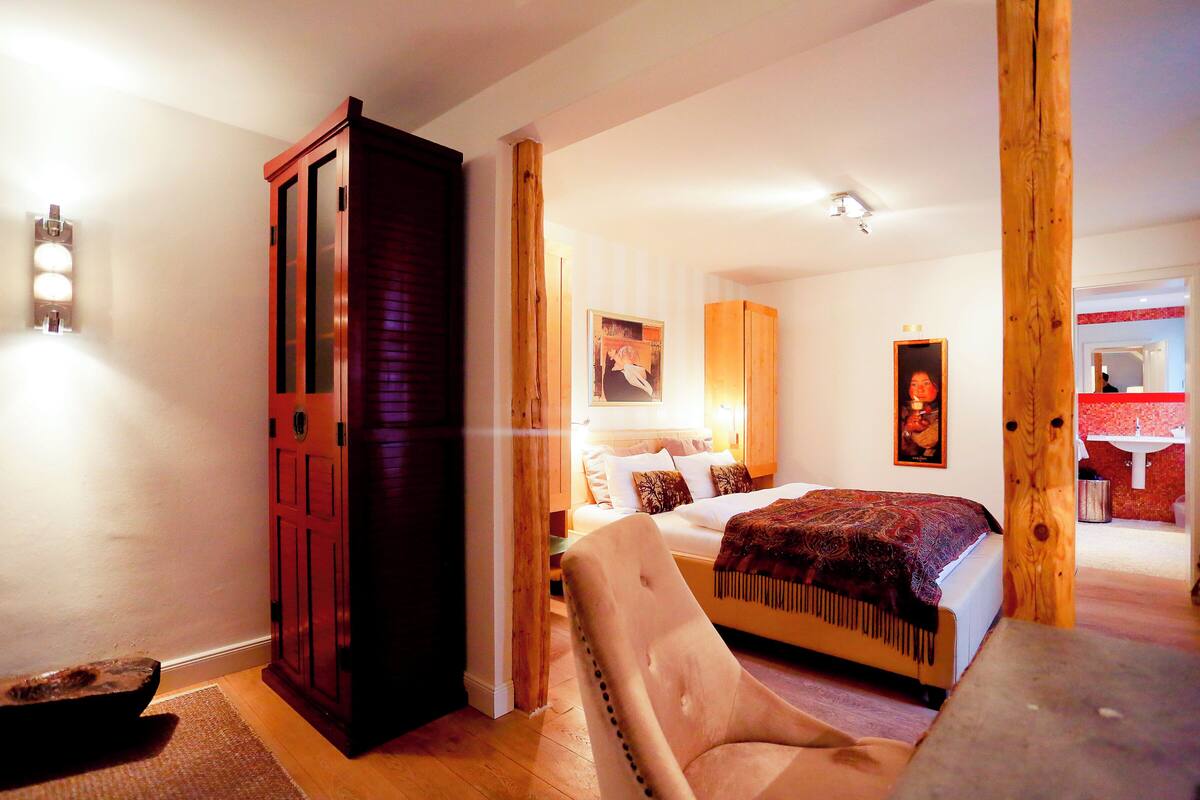 A bedroom with a bed, a wooden wardrobe, a chair, and a desk.